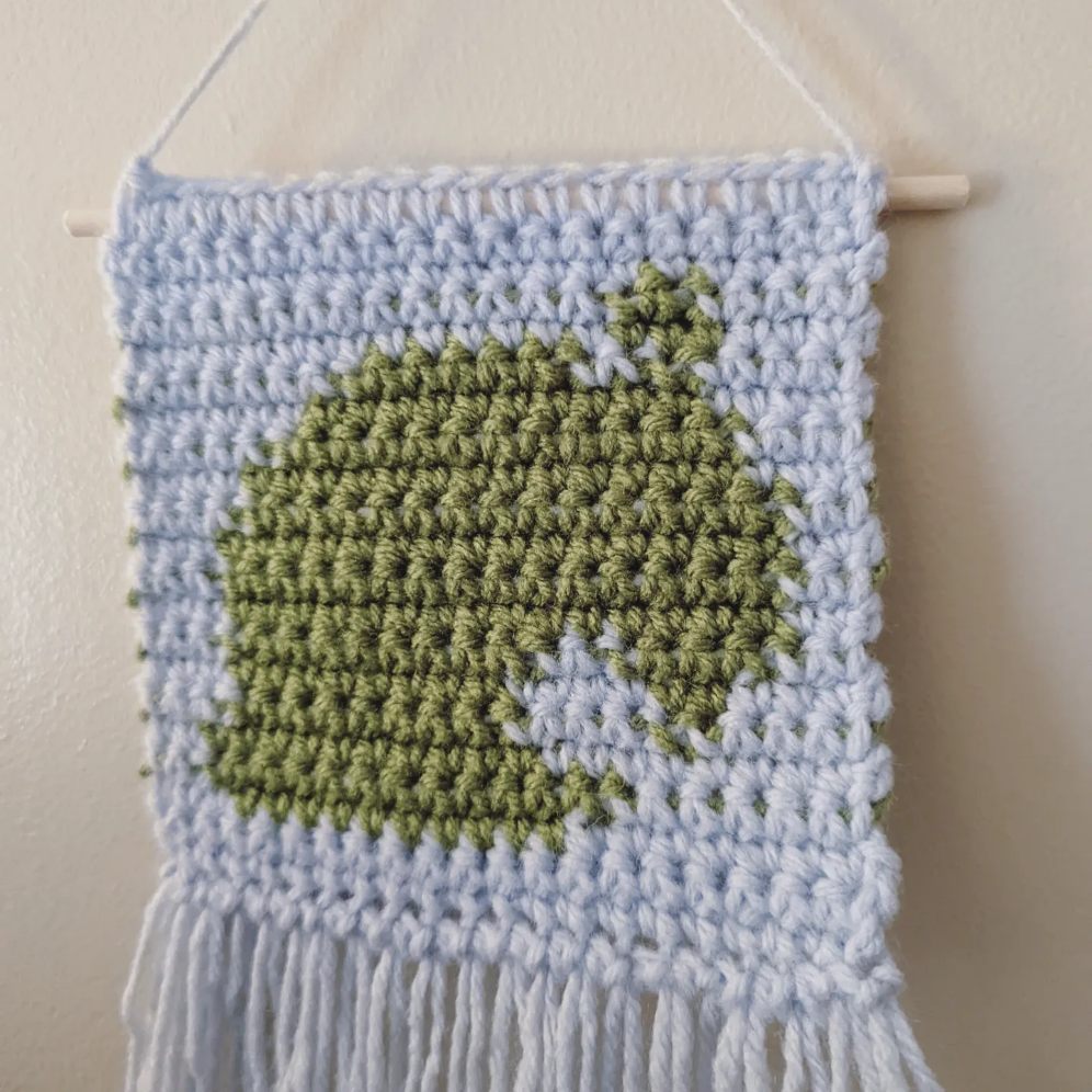Crochet Tapestry with a Green Animal Crossing leaf on a baby blue background